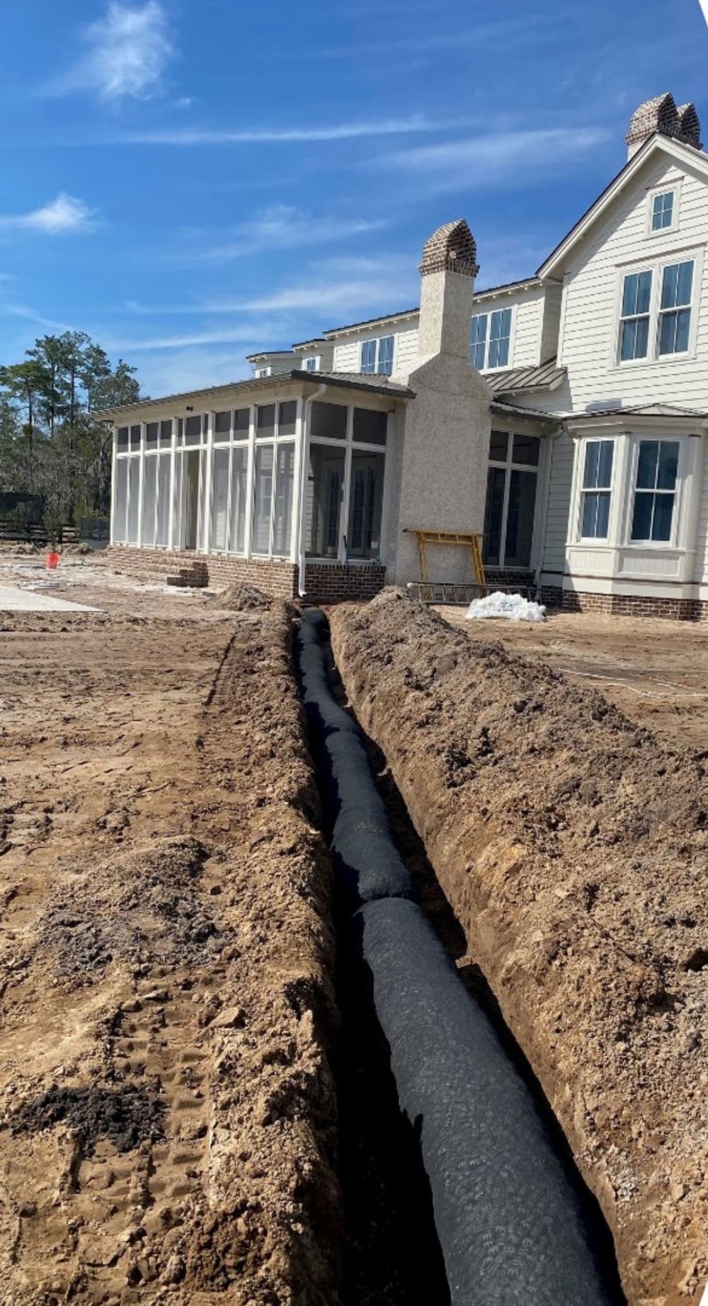 Excavated trench for drainage pipeline installation beside a newly constructed house.