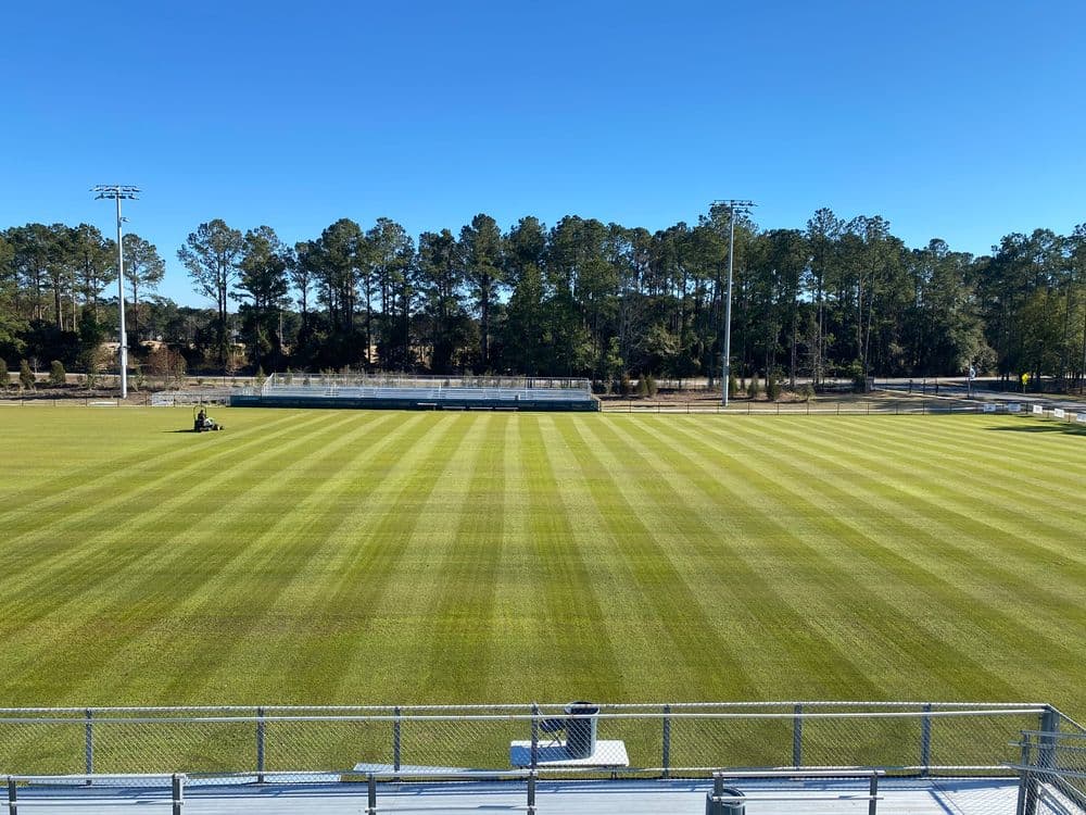 Well-maintained soccer field with striped grass, bleachers, and clear blue sky.