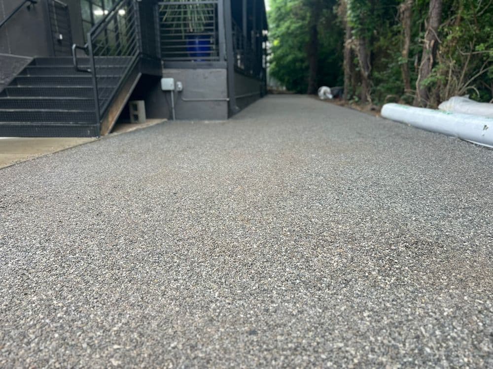 Newly paved walkway alongside a building, surrounded by greenery and construction materials.