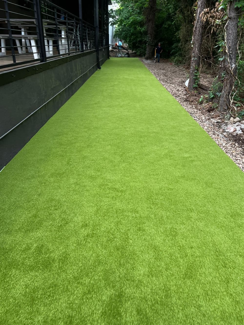 Lush green artificial turf pathway surrounded by trees and a building.