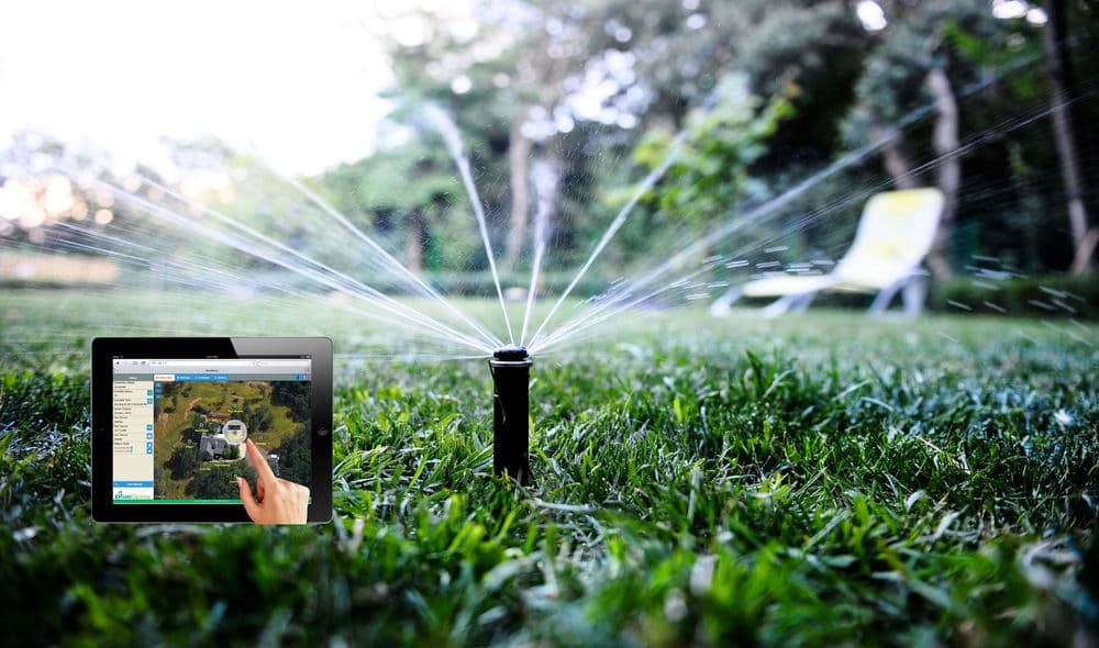 Smart irrigation system with a tablet controlling lawn sprinkler in a lush green yard.